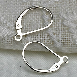 Op de afbeelding: Twee zilveren oorhaken met een veerclip sluiting. De haken zijn gemaakt van metaal en hebben een glanzende afwerking.