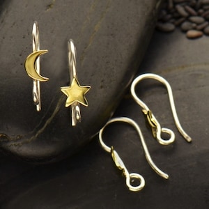 May include: A set of three silver earring hooks. Two of the hooks have a gold crescent moon and a gold star charm attached. The third hook is plain.
