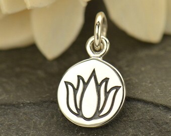 May include: A silver charm with a black lotus flower design. The charm is round and has a loop at the top for attaching to a necklace or bracelet.