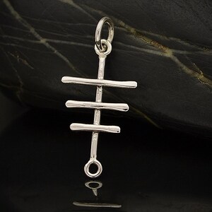 May include: Silver charm pendant featuring a stylised cross design. The cross is made of three horizontal bars connected to a vertical bar.