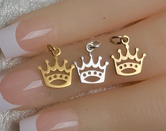 May include: Three gold, silver, and gold-toned crown charms. The charms are in the shape of a crown with a pointed top and five points on each side. The charms are on a hand with painted nails.