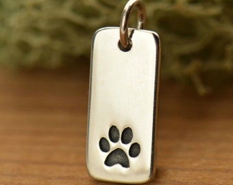 May include: A rectangular sterling silver pendant with a paw print design. The pendant has a polished finish and a small loop at the top for a chain. The words "Sterling Silver" are printed at the bottom.