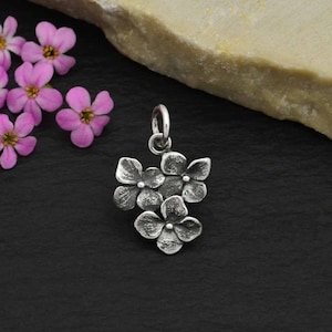 May include: A silver charm featuring a cluster of five delicate, textured flowers. The flowers are arranged in a cascading pattern, creating a delicate and feminine look.