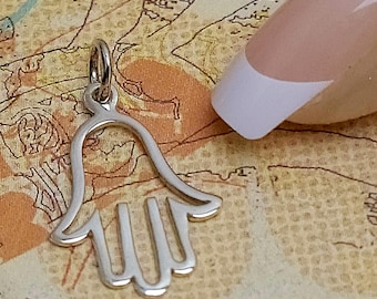 Puede incluir: Un dije de mano de Hamsa de color plateado con un lazo para colgar. El dije es un diseño de mano abierta estilizada, con tres dedos y un pulgar visibles. El fondo es un mapa vintage.