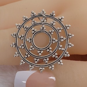 May include: A silver pendant with a circular design. The pendant has three concentric circles with a rope-like texture and small, beaded accents. A small loop is at the top for hanging.