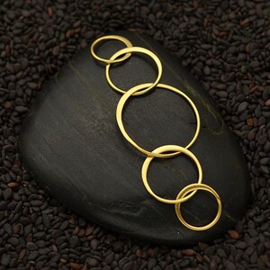 May include: A set of five gold-toned interlocking rings, arranged in a cascading pattern, on a black stone surface.