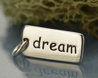 May include: A silver charm with the word "dream" engraved on it. The charm has a loop for attaching to a bracelet or necklace.