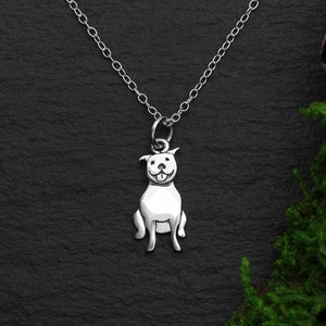 May include: A silver necklace with a charm of a sitting dog. The dog is smiling with its tongue sticking out.