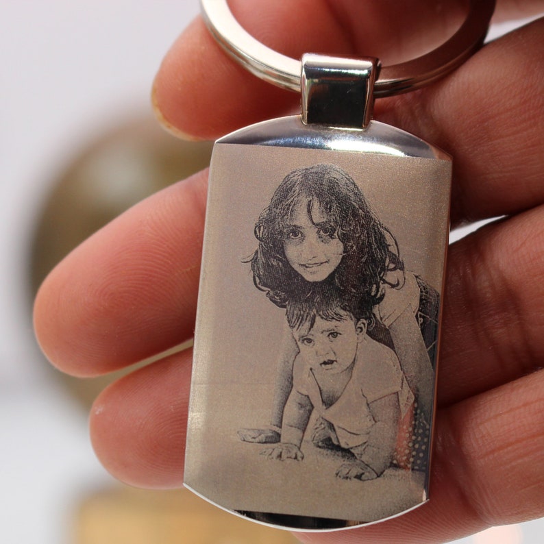 May include: A silver keyring with a rectangular tag featuring an engraved image of two children. The older child is a girl with long hair, and the younger child is a boy with short hair. Both children are smiling.