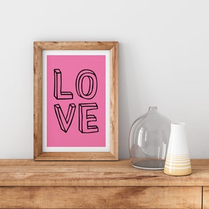 Può includere: Una stampa incorniciata con uno sfondo rosa e la parola "LOVE" scritta in lettere nere delineate. Le lettere sono stilizzate e sembrano essere tridimensionali.