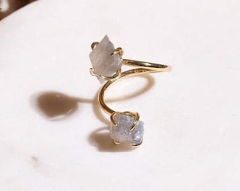 May include: A gold ring with two raw, grey, crystal stones. The ring is a simple, minimalist design.