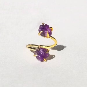 May include: A gold ring with two purple amethyst stones. The ring is designed with a twisted band.