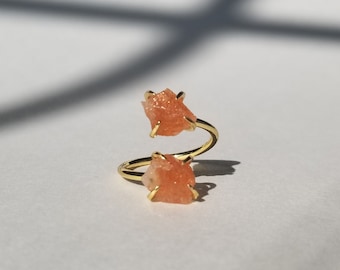May include: A gold ring with two orange sunstone crystals. The ring is a spiral design.