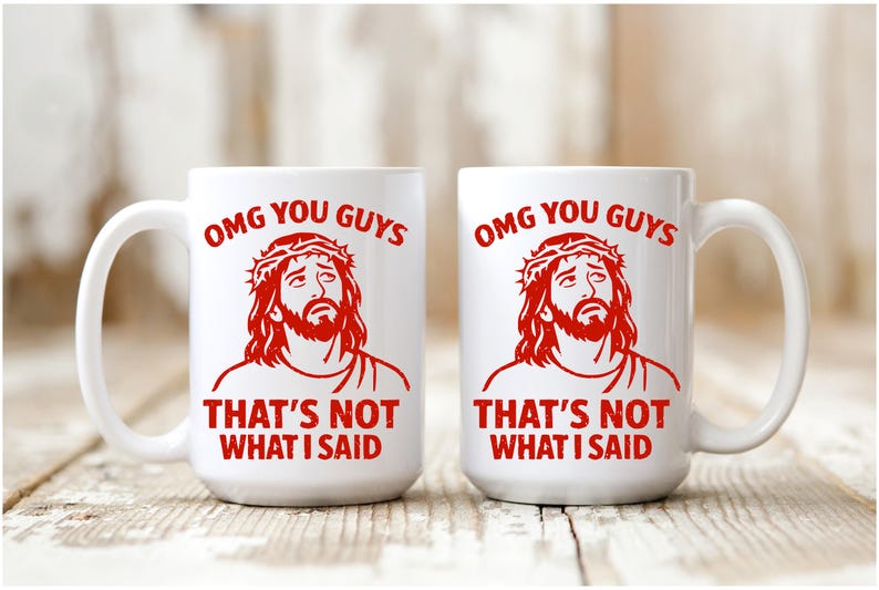 Pu&ograve; includere: Due tazze di ceramica bianca con una grafica rossa di una persona con una corona di spine. Le tazze hanno il testo "OMG YOU GUYS" e "THAT'S NOT WHAT I SAID" in rosso. Le tazze sono su una superficie di legno.