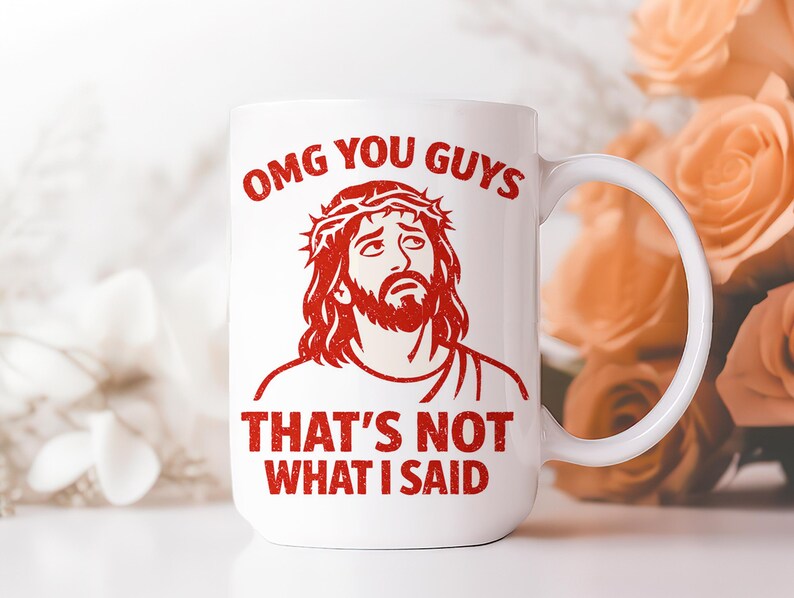 Pu&ograve; includere: Tazza in ceramica bianca con grafica rossa di un uomo con corona di spine e la scritta "OMG YOU GUYS THAT'S NOT WHAT I SAID". La tazza ha un manico curvo. Lo sfondo &egrave; sfocato.