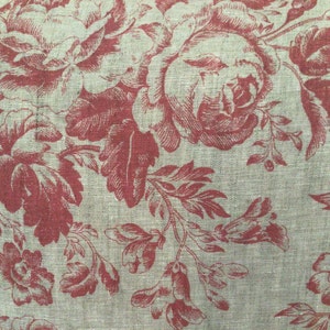 May include: Close-up of a fabric with a floral pattern. The design features large, stylized red roses and other flowers with green leaves and stems against a light gray background. The fabric has a textured appearance.