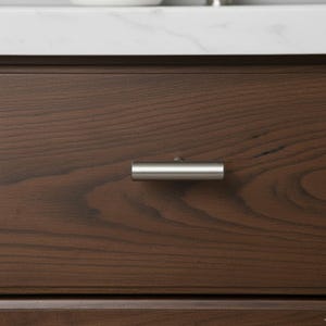 May include: Close-up of a dark brown wooden drawer with a brushed nickel cylindrical handle. The drawer is part of a larger cabinet or dresser. The handle is horizontally mounted and centered on the drawer front.