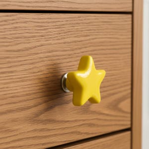 May include: A bright yellow star-shaped drawer pull is mounted on a wooden drawer. The drawer pull has a glossy finish and a silver-colored base. The wood grain of the drawer is visible.