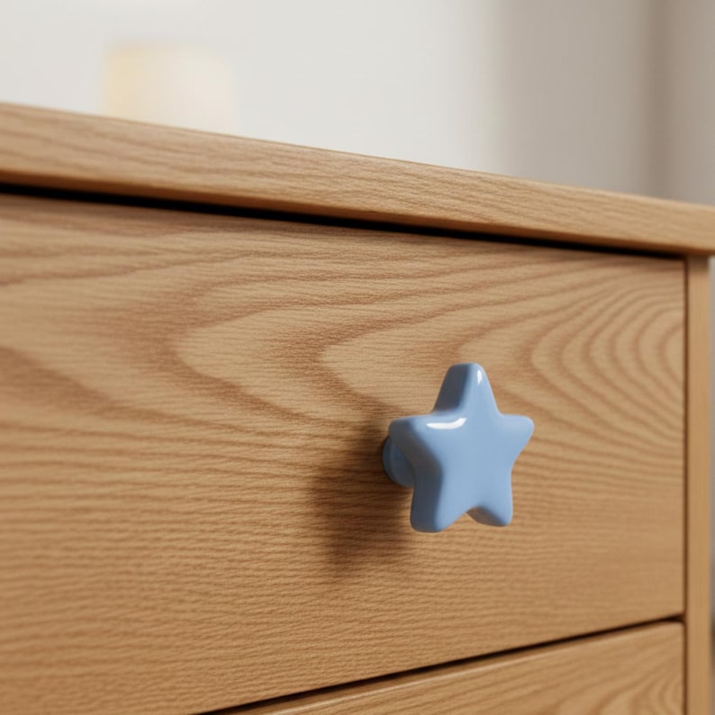 Puede incluir: Tirador en forma de estrella azul claro en un mueble de madera. El mueble tiene un acabado de veta de madera natural. El tirador es un acento decorativo en el frente del caj&oacute;n.