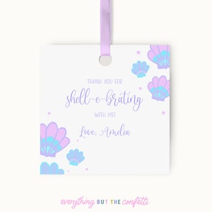 May include: A white thank you tag with a purple ribbon. The tag has a purple and blue seashell design with stars. The text reads "Thank you for shell-e-brating with me! Love, Amelia".