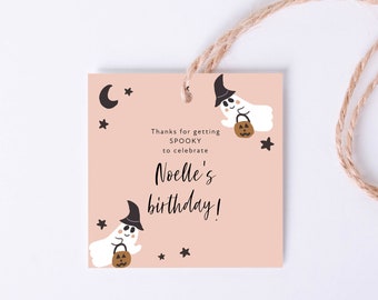 May include: A square, light pink gift tag with a Halloween theme. The tag features illustrations of ghosts, stars, and a crescent moon. Text on the tag reads "Thanks for getting SPOOKY to celebrate Noelle's birthday!" A natural twine string is attached.