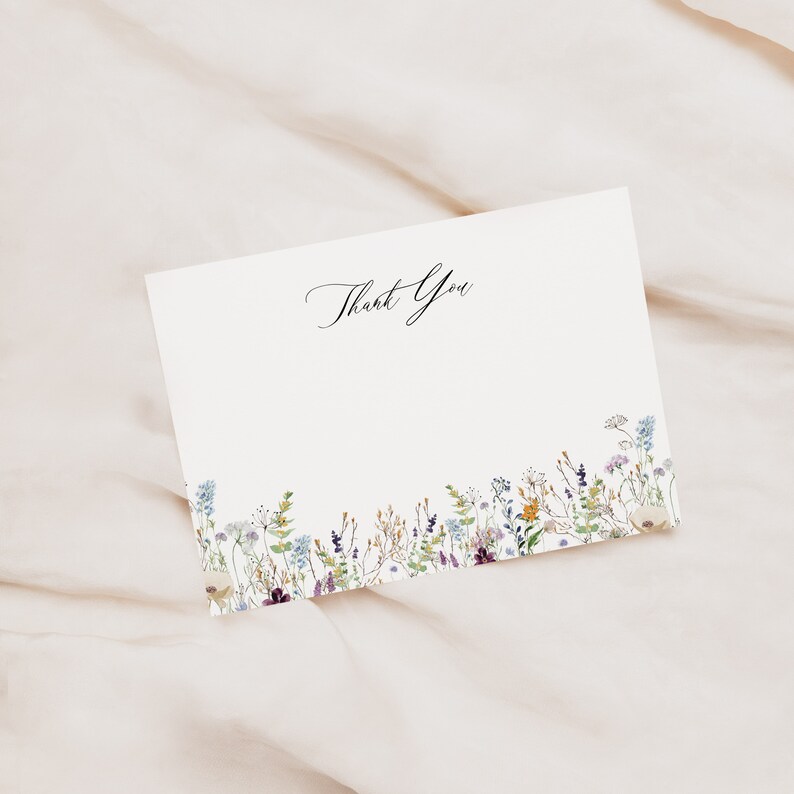 Op de afbeelding: Een witte bedankkaart met een bloemige rand. De bloemen zijn in tinten paars, blauw, geel en groen. De tekst "Bedankt" staat in zwarte cursieve letters.
