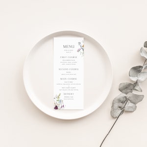 Op de afbeelding: Een huwelijksmenukaart met een bloemenontwerp. Het menu bevat de volgende gangen: Voorgerecht, Veldgroentesalade; Hoofdgerecht, Risotto; Hoofdmaaltijd, Biefstuk of Wilde Zalm; Dessert, Trouwtaart.