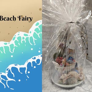 May include: A gift basket with a beach theme, wrapped in clear cellophane. The basket includes a small teacup filled with decorative items, seashells, and a small stuffed animal. The words "Beach Fairy" are visible in the image.