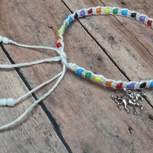 May include: A white string bracelet with rainbow colored beads and a silver unicorn charm. The bracelet has white beads on the ends of the strings.