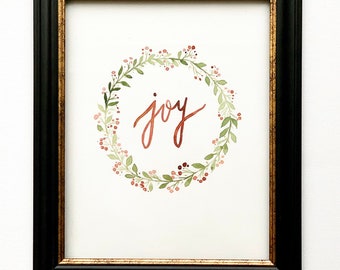 May include: A framed watercolor painting of a floral wreath with the word "joy" written in copper-colored script.