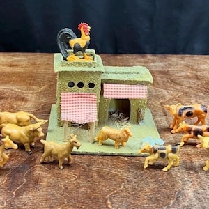 Puede incluir: Una escena de granja en miniatura con un granero, un gallo, caballos, vacas y cabras. El granero es verde con un toldo a cuadros rojos y blancos. Los animales son de varios tonos de amarillo, marrón y negro.