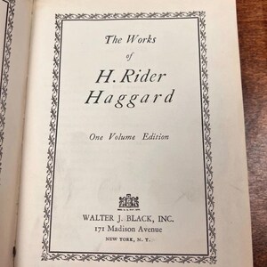 以下が含まれることがあります： 「The Works of H. Rider Haggard」のタイトルページが表示された開いた本。テキストは黒色で、オフホワイトのページに書かれており、装飾的なボーダーで囲まれています。ニューヨークの住所を含む出版社の情報も表示されています。