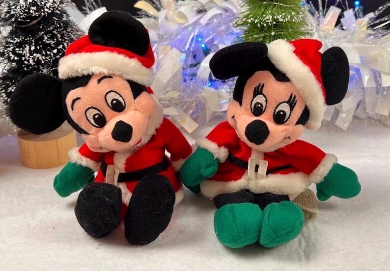 K&ouml;nnte beinhalten: Zwei Pl&uuml;schpuppen von Mickey Mouse und Minnie Mouse in Weihnachtsmann-Outfits. Jede Puppe tr&auml;gt eine rote Jacke mit wei&szlig;em Besatz, einen schwarzen G&uuml;rtel und einen Weihnachtsmannhut. Sie haben gr&uuml;ne Handschuhe und Schuhe.