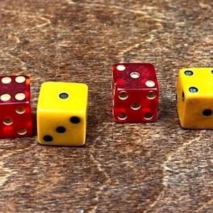 May include: Four dice in a row, two red and two yellow, with black dots indicating the numbers. The dice are on a wooden surface. The red dice have white dots. The yellow dice have black dots.