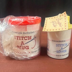 K&ouml;nnte beinhalten: Zwei Kunststoff-Bastelbeh&auml;lter mit wei&szlig;er Netzau&szlig;enseite f&uuml;r Handarbeiten. Der linke Beh&auml;lter hat einen roten Deckel und ein Etikett mit der Aufschrift STITCH A MUG. Der rechte hat einen gelben Deckel, ein Crafter's Pride-Etikett und die Aufschrift STITCH A SIPPER.