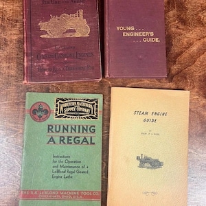 Puede incluir: Cuatro libros antiguos sobre una superficie de madera. Los títulos incluyen "The Traction Engine", "Young Engineer's Guide", "Running a Regal" y "Steam Engine Guide". Los libros son de varios colores, con ilustraciones de maquinaria.