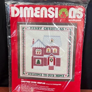 May include: A Dimensions needlepoint kit titled Christmas Home Sampler in a clear plastic bag. The package features a red background with a printed design of a house, the text Merry Christmas, and Welcome to Our Home. It measures 18 by 18 inches.
