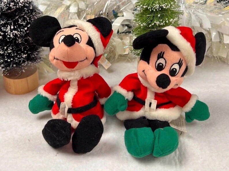 K&ouml;nnte beinhalten: Zwei Pl&uuml;schfiguren von Mickey und Minnie Mouse in Weihnachtsmann-Outfits. Jede Figur tr&auml;gt eine rote Jacke mit wei&szlig;em Besatz, einen schwarzen G&uuml;rtel, gr&uuml;ne Handschuhe und einen Weihnachtsmannhut. Die Figuren sind schwarz, rot, wei&szlig; und gr&uuml;n.