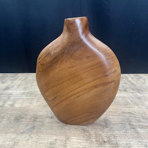 May include: A handcrafted wooden vase with a smooth, rounded body and a narrow neck. The vase is made of light brown wood, showcasing natural grain patterns. The vase has a polished finish and is suitable for displaying flowers or as a decorative item.