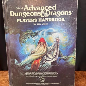 May include: A vintage "Advanced Dungeons & Dragons Players Handbook" by Gary Gygax. The cover features a wizard with a long white beard, a red hat, and a flowing white robe, set against a blue and purple background with fantasy creatures.