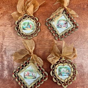 May include: Four decorative photo frames in gold with red and green detailing, each with a small vintage image and a sheer gold ribbon. The frames are in various shapes, including round and diamond. The frames are made of metal.