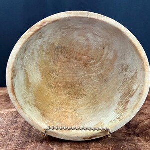 May include: A handcrafted wooden bowl with a natural finish. The bowl has a round shape with a wide opening and a visible wood grain pattern. The bowl is supported by a decorative metal stand.