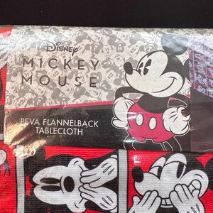 以下が含まれることがあります： ミッキーマウスをテーマにしたテーブルクロス。テーブルクロスは、ミッキーマウスの顔と体の繰り返し模様が赤と黒の背景に描かれています。ディズニーのロゴと「ミッキーマウス」がテーブルクロスの上部に印刷されています。