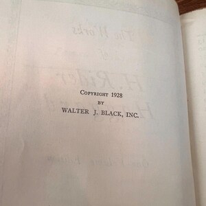 以下が含まれることがあります： テキストが書かれた開いた本のページ。ページには、セリフフォントで「Copyright 1928 by Walter J. Black, Inc.」と書かれています。紙は薄茶色で古くなっており、本は木の表面に開かれています。