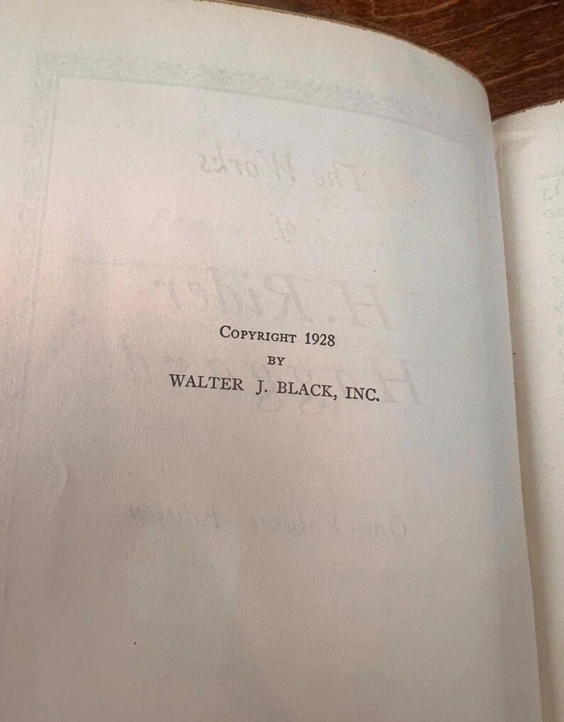 以下が含まれることがあります： テキストが書かれた開いた本のページ。ページには、セリフフォントで「Copyright 1928 by Walter J. Black, Inc.」と書かれています。紙は薄茶色で古くなっており、本は木の表面に開かれています。