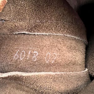 May include: Close-up of the interior of a brown leather item. The texture is rough and fuzzy. White numbers "6018 02" are visible on the leather. The item appears to be a boot or shoe.