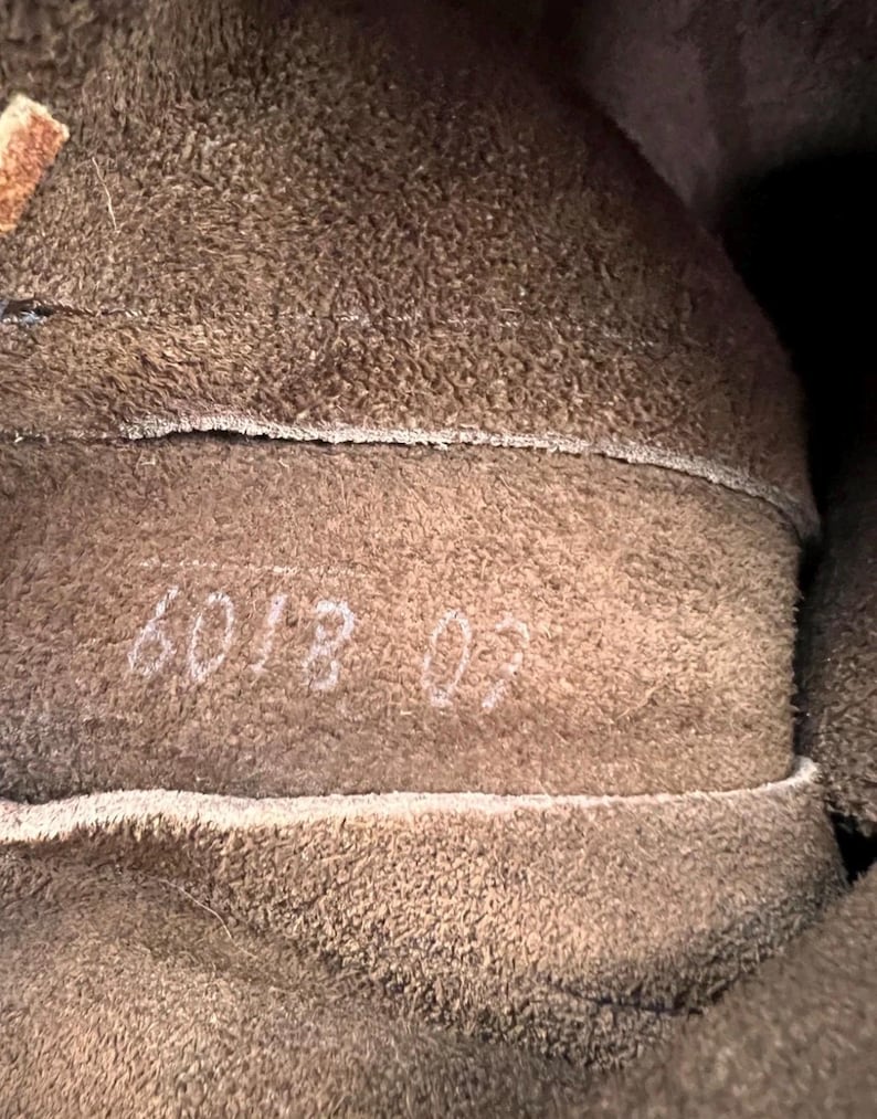 May include: Close-up of the interior of a brown leather item. The texture is rough and fuzzy. White numbers "6018 02" are visible on the leather. The item appears to be a boot or shoe.