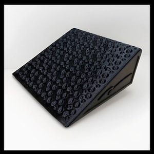 May include: A black, angled wedge with a textured surface of repeating, rounded shapes. The object is made of a solid material and sits on a white surface. The design is modern and geometric.