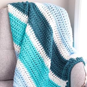 Può includere: Una coperta all'uncinetto con strisce blu, turchese, bianche e azzurro. La coperta è drappeggiata su una poltrona grigia.