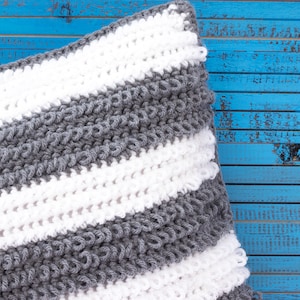 May include: A gray and white striped knitted pillow with a textured surface. The pillow is on a blue wooden background.